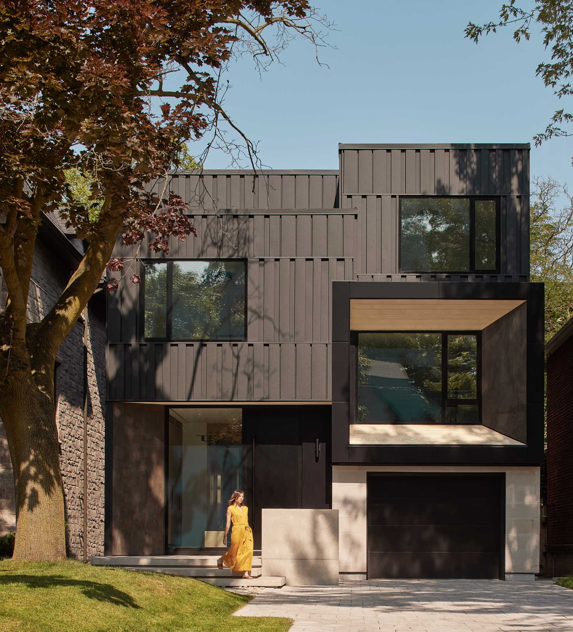 The exterior of this modern home is composed of a series of interlocking volumes, with the upper storeys set back to provide a gentle transition from street level. Clad in rhythmically patterned black metal, the facade is accentuated by warm wood siding and porcelain slabs.